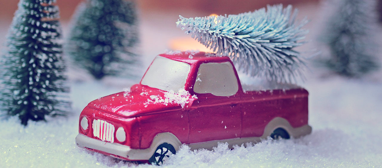 Ein rotes Spielzeugauto steht in einer Winterlandschafts und hat einen verschneiten Weihnachtsbaum auf dem Dach.
